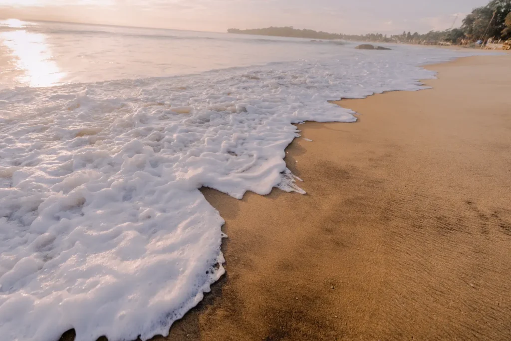 white foamy waves washing over golden sand at sunrise.