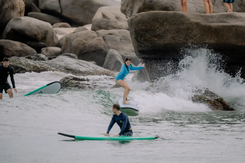people learning to surf on a rocky beach with waves.